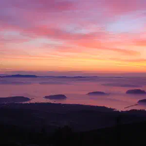 A dramatic pink and orange sunrise sky over Frenchman Bay with forested islands silhouetted in the distance.