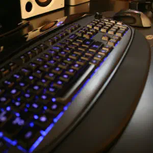 A black keyboard with blue LED backlighting glowing beneath the keys on a dark desk with desktop speakers and a wireless mouse in the background.