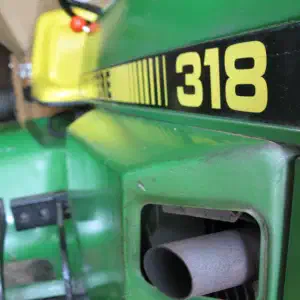 A close-up view of green machinery with a yellow and black label reading '318' and a yellow measuring tape in the background.