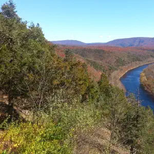 A winding blue river flows through a forested valley surrounded by rolling mountains and autumn-colored trees under a clear sky.