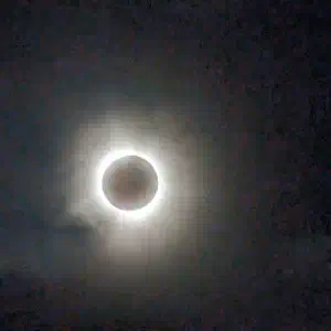 A total solar eclipse with the moon blocking the sun's disk, revealing the sun's corona as a glowing white halo against a darkened sky.