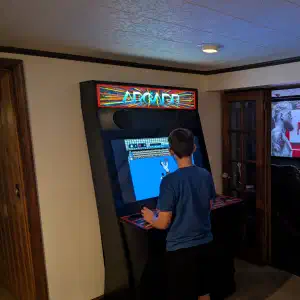 A person plays an arcade game in a dimly lit room while a television screen displays a Netflix boxing documentary in an adjoining area.