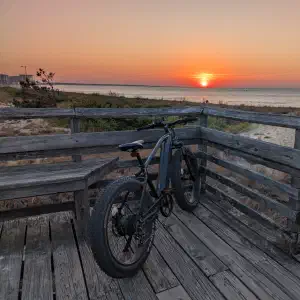 Fat tire electric bike parked on a weathered wooden boardwalk overlooking the ocean with a golden sunset on the horizon