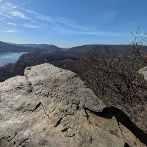 Sunlit rock outcrop with old carved inscriptions overlooking the Potomac River winding through forested mountains on a clear winter day